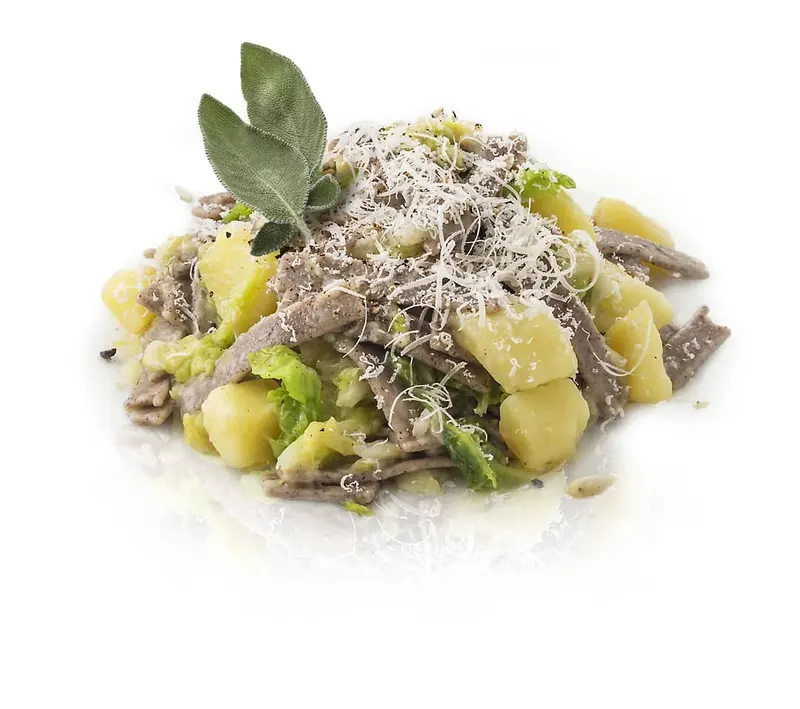 Un piatto di pizzoccheri con le patate, la verza, il formaggio grattugiato e una foglia di salvia