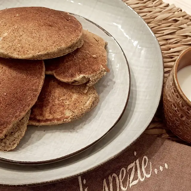 Una pila di pancake di grano saraceno in un piatto, con una tazza di latte
